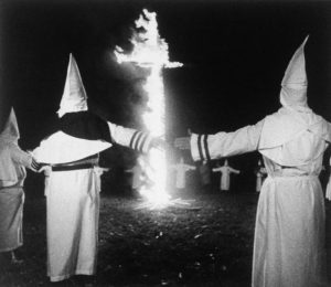 Hooded and robed members of the Ku Klux Klan hold their hands apart as they rally around a 15 foot high burning cross in Ephrata, Pennsylvania Saturday, Oct. 3, 1987. (AP Photo/Bill Cramer)